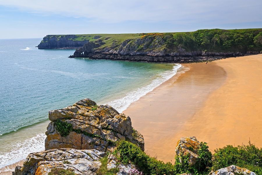 A beach with a large rock in the foreground and a cliff in the background.