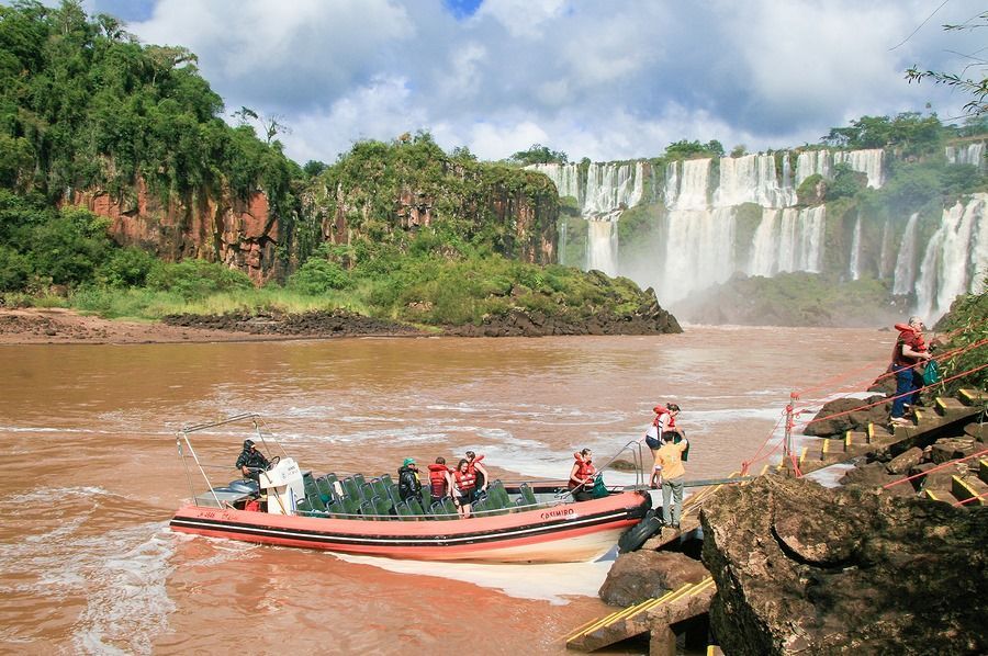 A boat full of people is going down a river near a waterfall.
