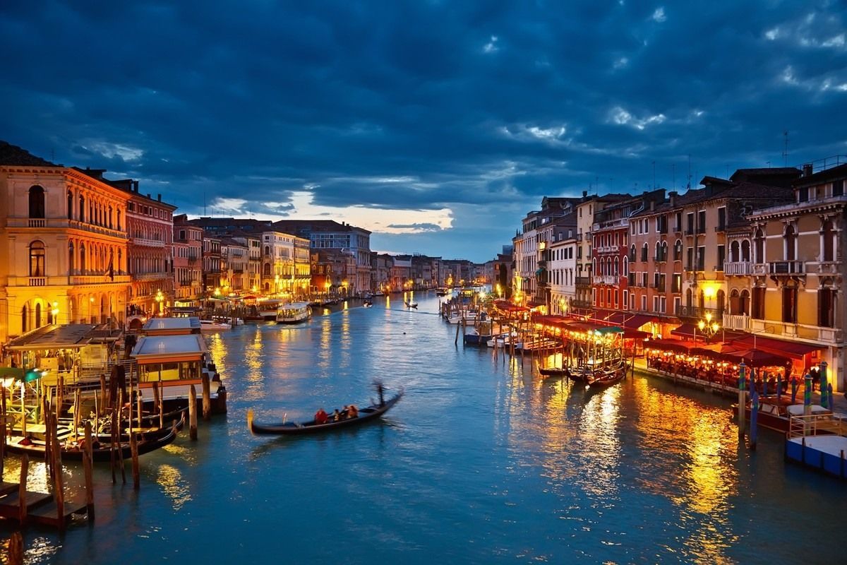 A gondola is floating down a canal in venice at night.
