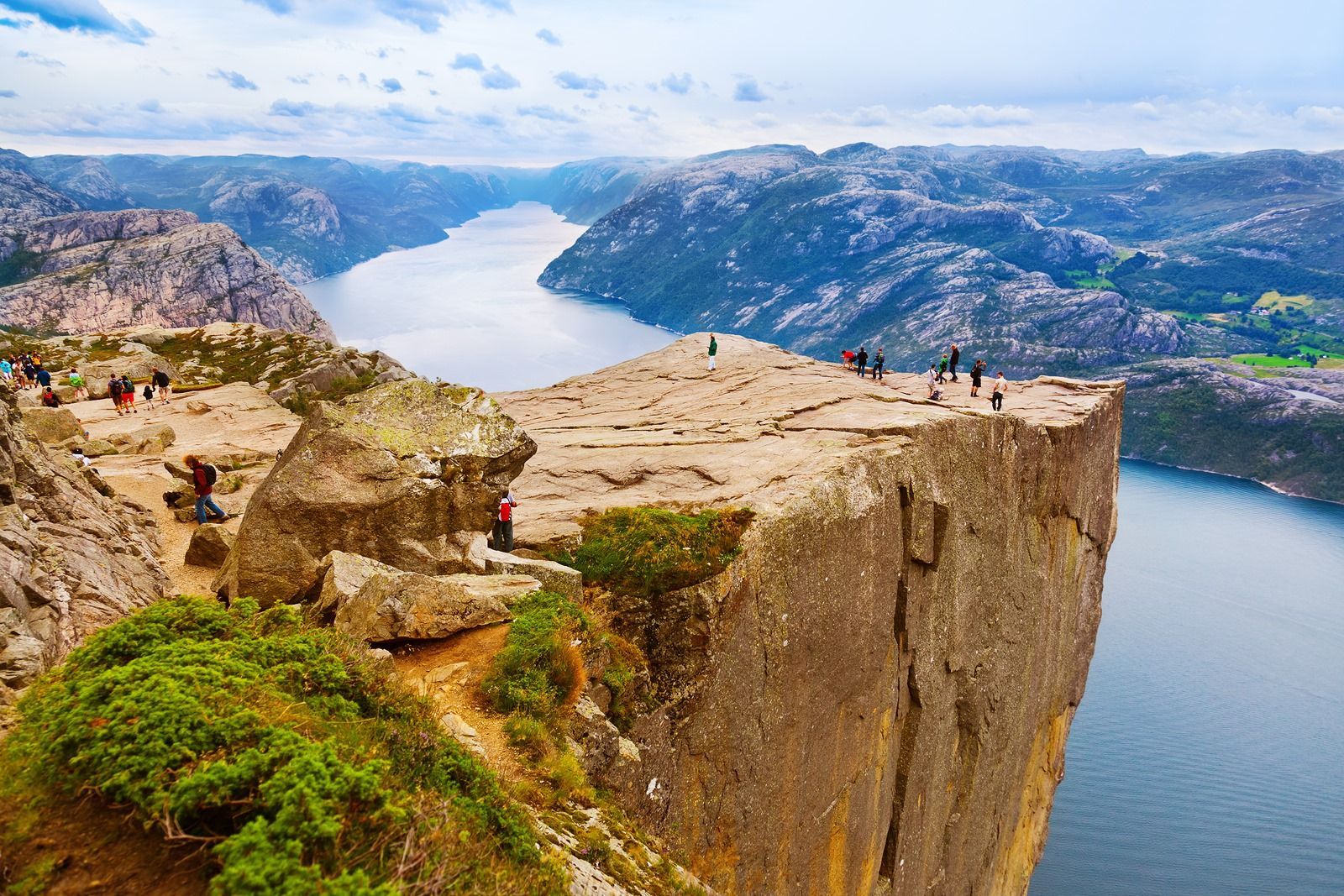 A group of people are standing on top of a cliff overlooking a lake.
