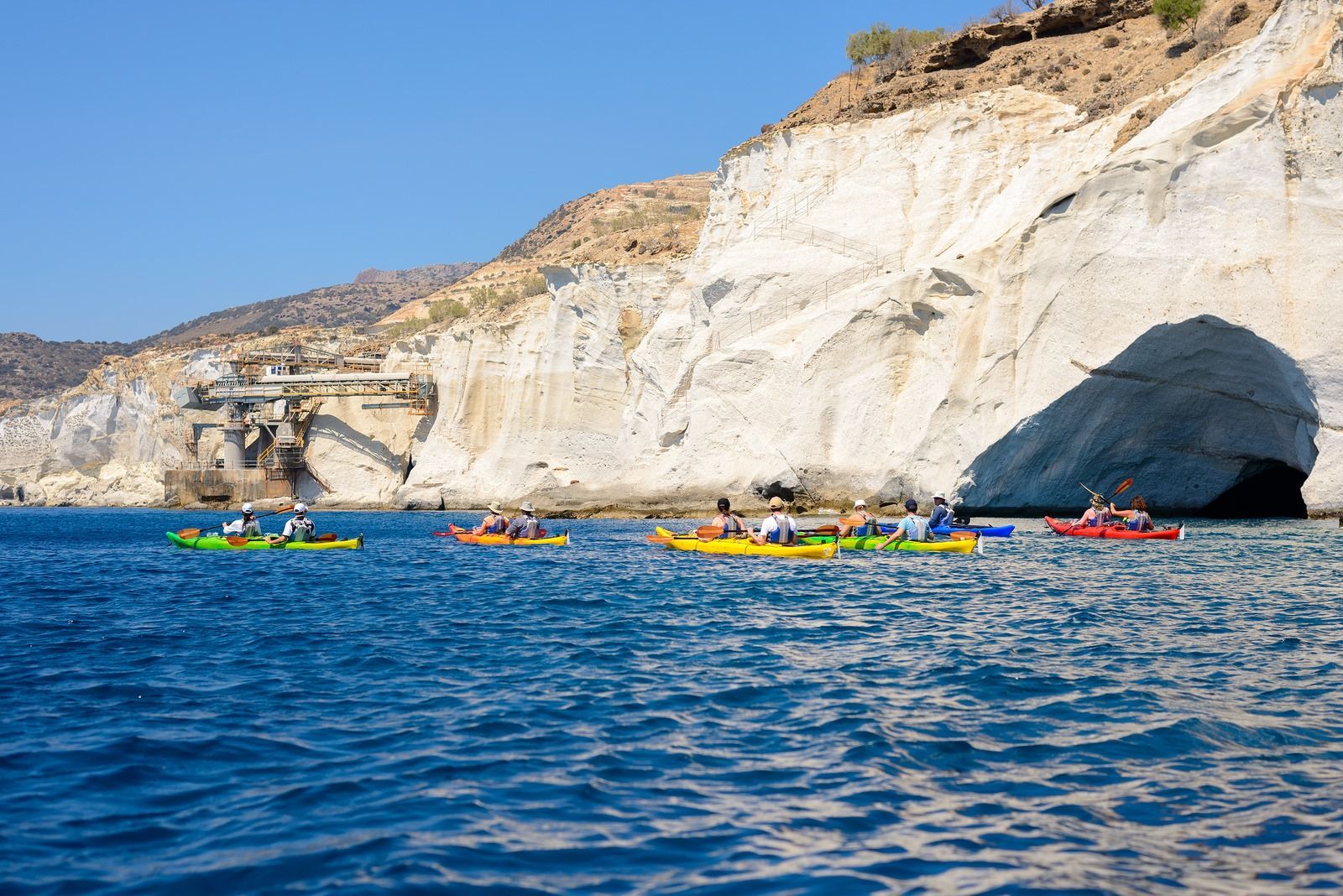 A group of people are kayaking in the ocean near a cave.