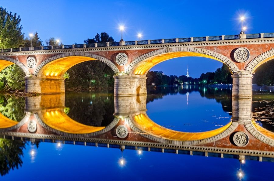 A bridge over a river at night with a reflection in the water.