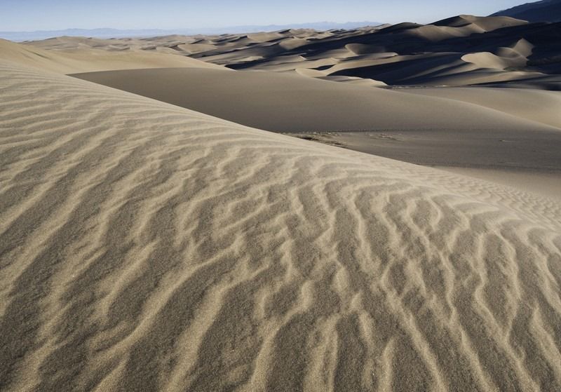 A sand dune in the desert with mountains in the background