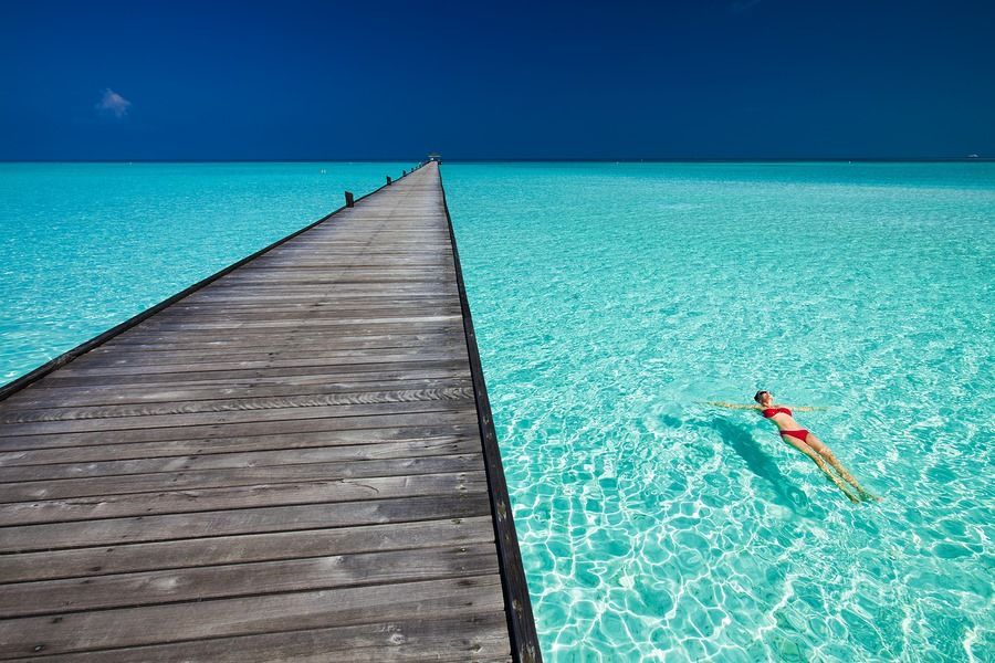 A woman is swimming in the ocean next to a wooden pier.