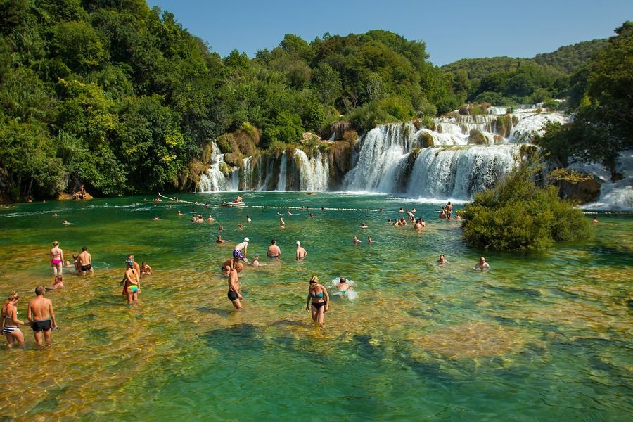 A group of people are swimming in a river near a waterfall.