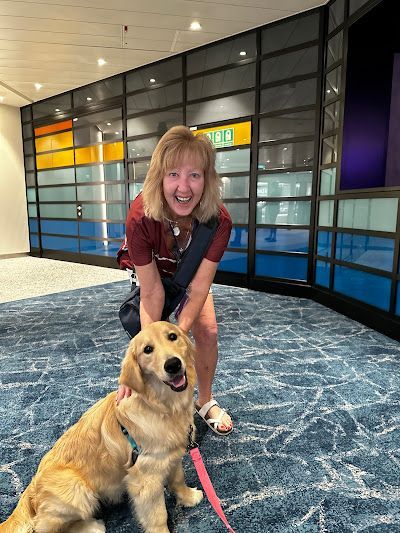 A woman is kneeling down next to a dog on a leash.