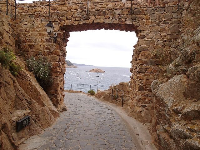 A stone archway over a cobblestone road leading to the ocean