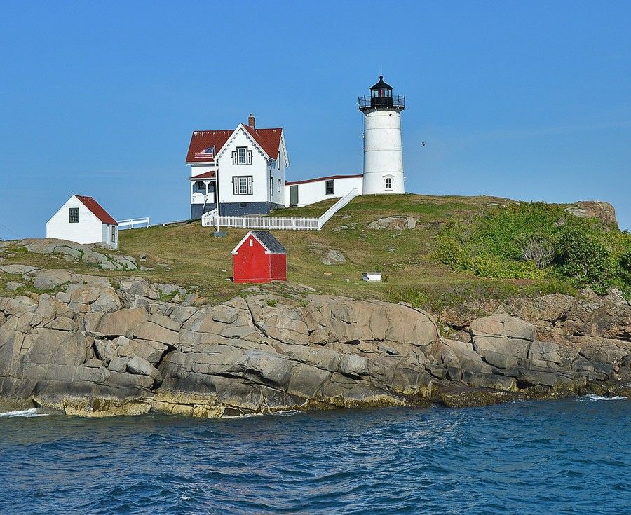 A lighthouse sits on top of a rocky hill near the water