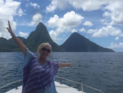 A woman is standing on a boat in the ocean with her arms outstretched.