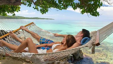 A man and a woman are laying in a hammock on the beach.