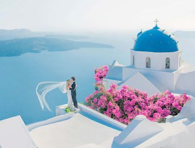 A bride and groom are standing on top of a building overlooking the ocean.