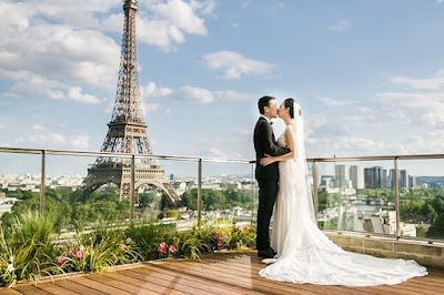A bride and groom are kissing on a balcony with the eiffel tower in the background.