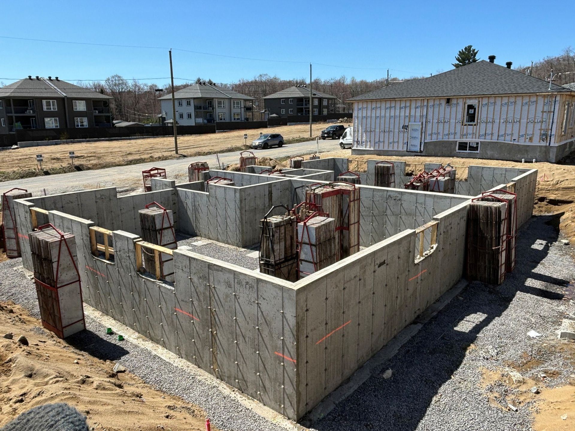Murs de fondation en construction, maisons voisines et ciel bleu.