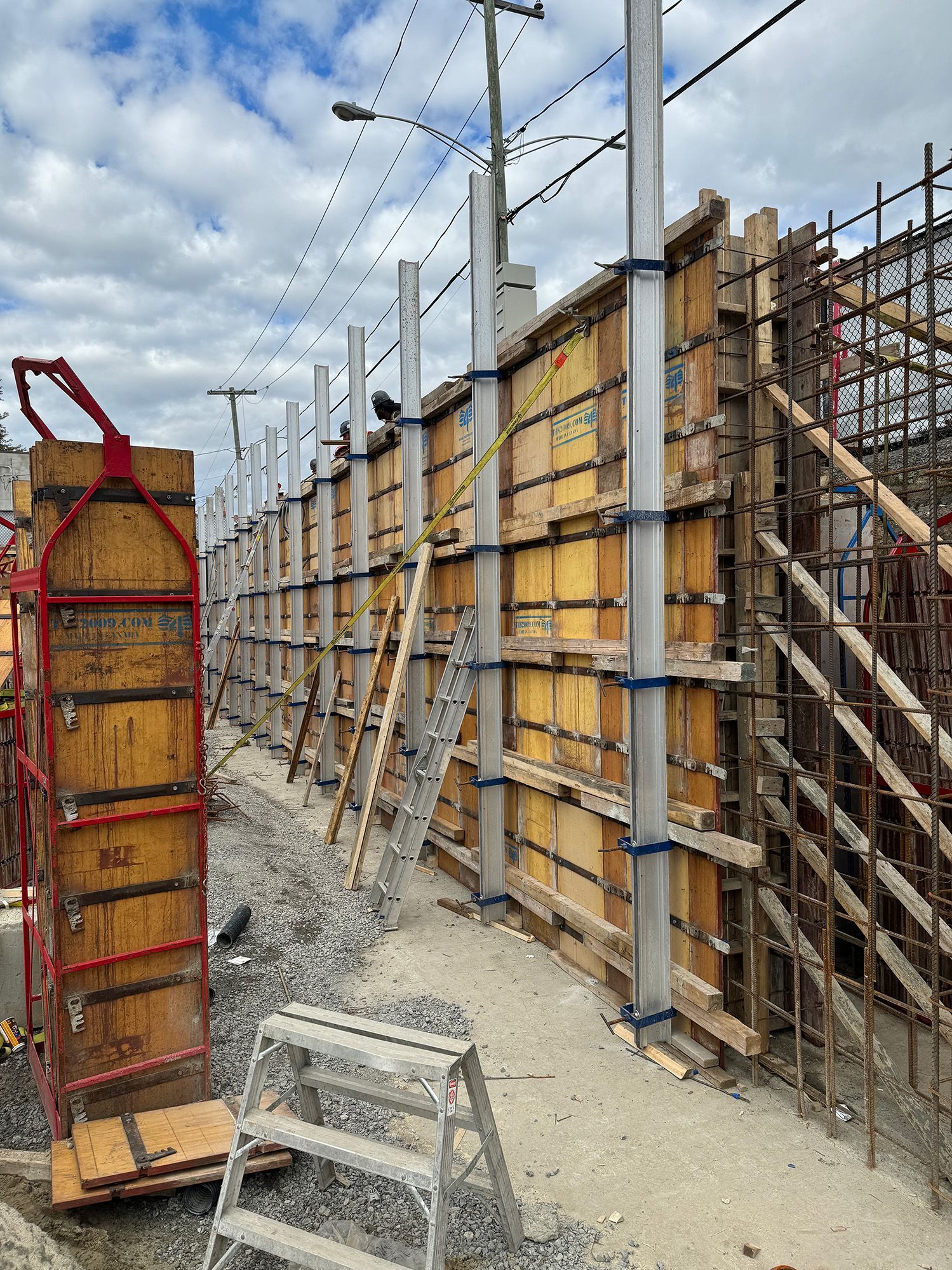 Chantier de construction avec coffrages en bois et supports métalliques pour un mur en béton.
