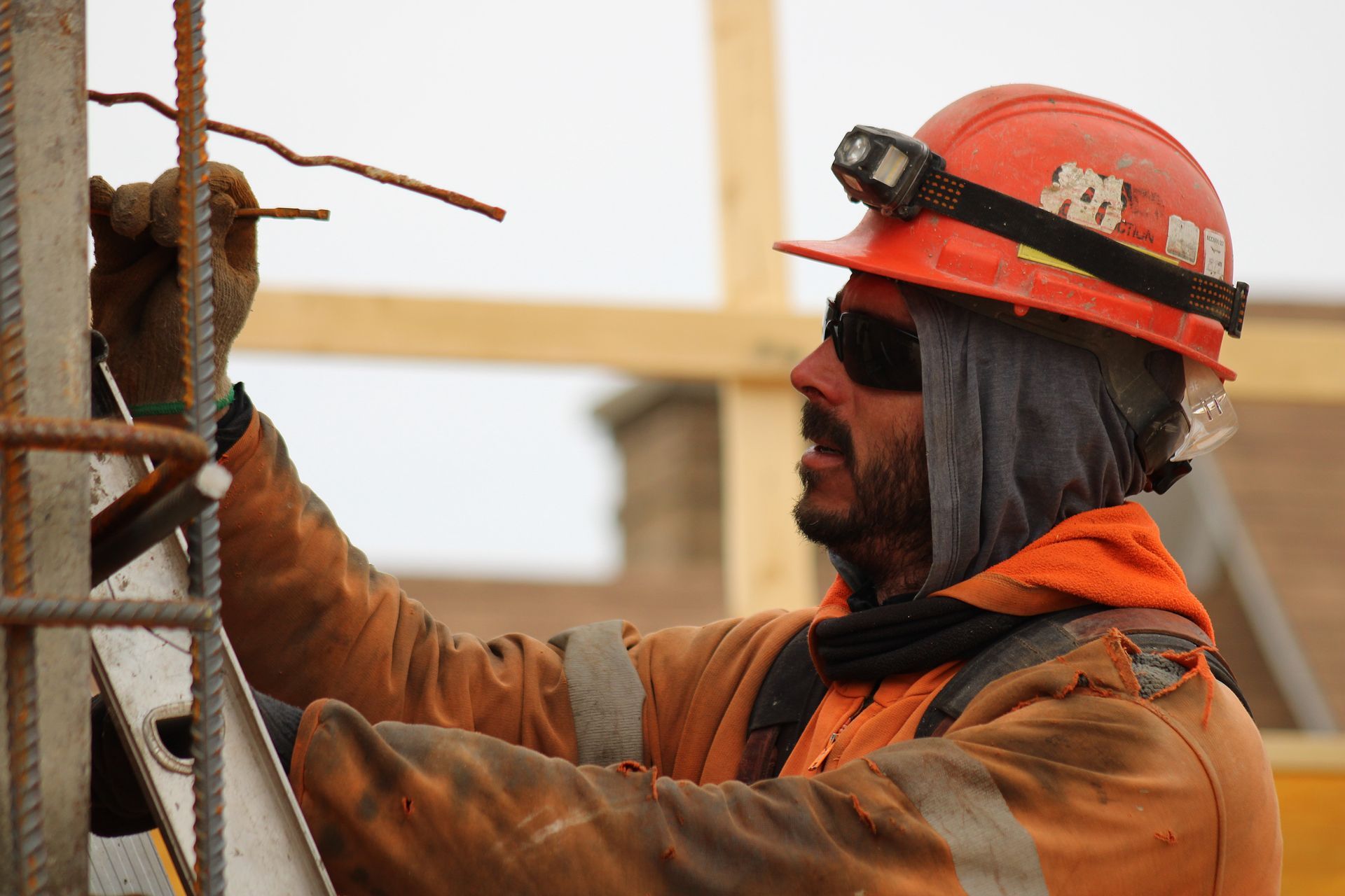 Ouvrier du bâtiment portant un casque orange et un gilet de sécurité, travaillant avec des barres d'armature.