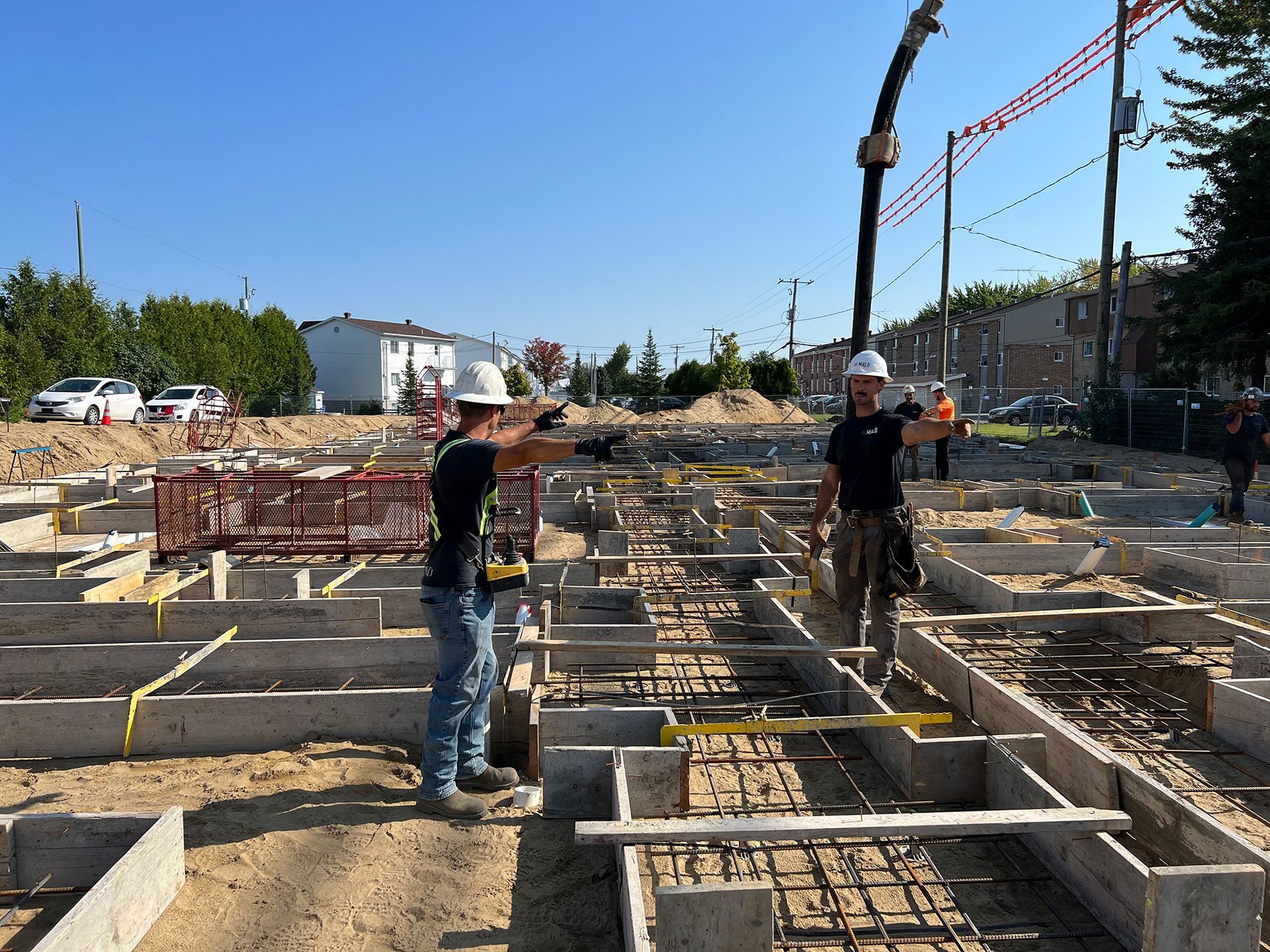 Des ouvriers du bâtiment manœuvrant une pompe à béton coulent le béton dans des coffrages sur un chantier. Ciel bleu.