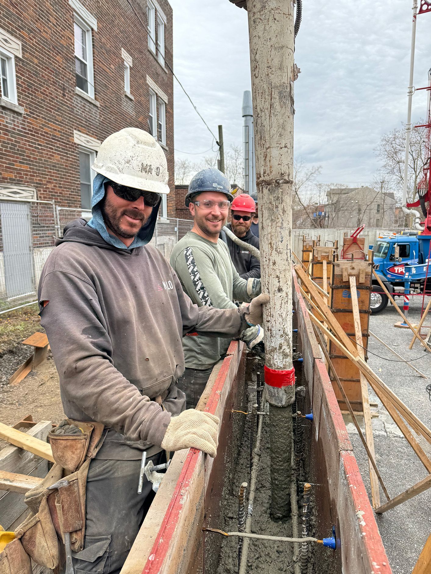 Des ouvriers du bâtiment coulent du béton dans un coffrage. Ils portent des casques et tiennent un tuyau. Un bâtiment se dresse en arrière-plan.