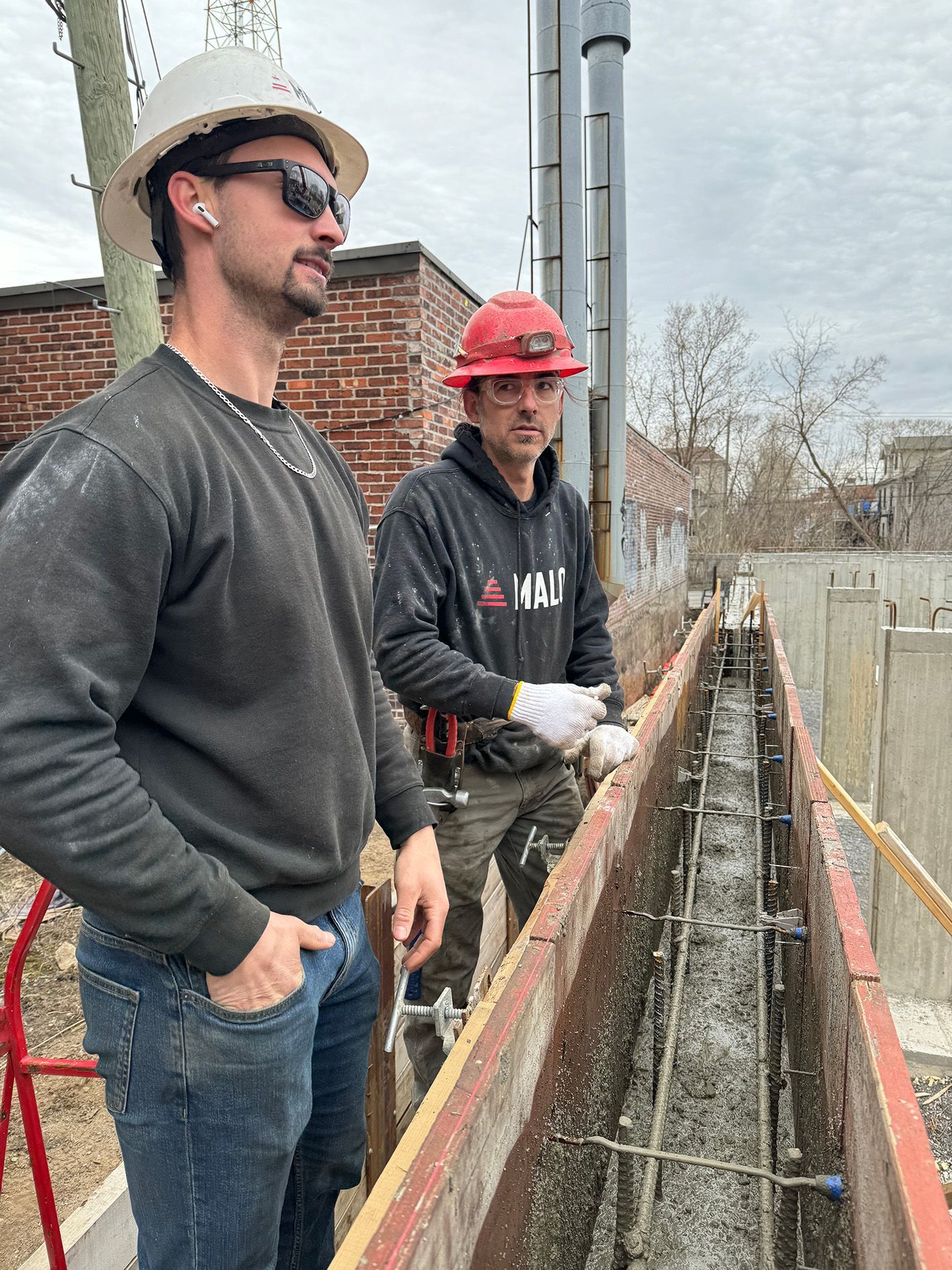 Deux ouvriers du bâtiment portant des casques de chantier inspectent à l'extérieur un coffrage en béton rempli d'armatures.