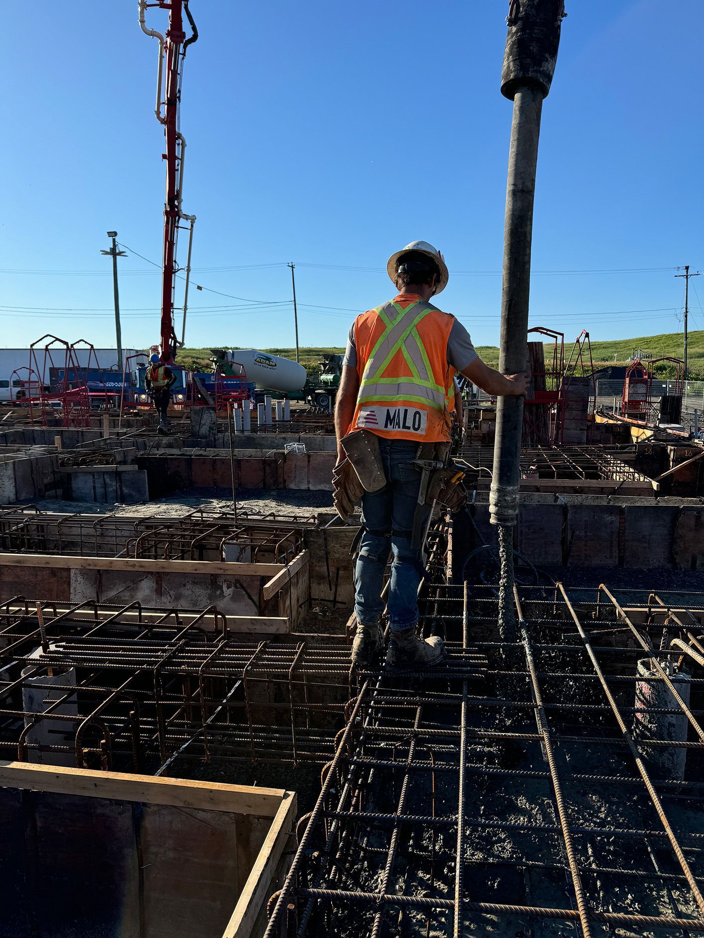 Ouvrier du bâtiment en gilet orange guidant le béton depuis la pompe, debout sur une armature en fer à béton.