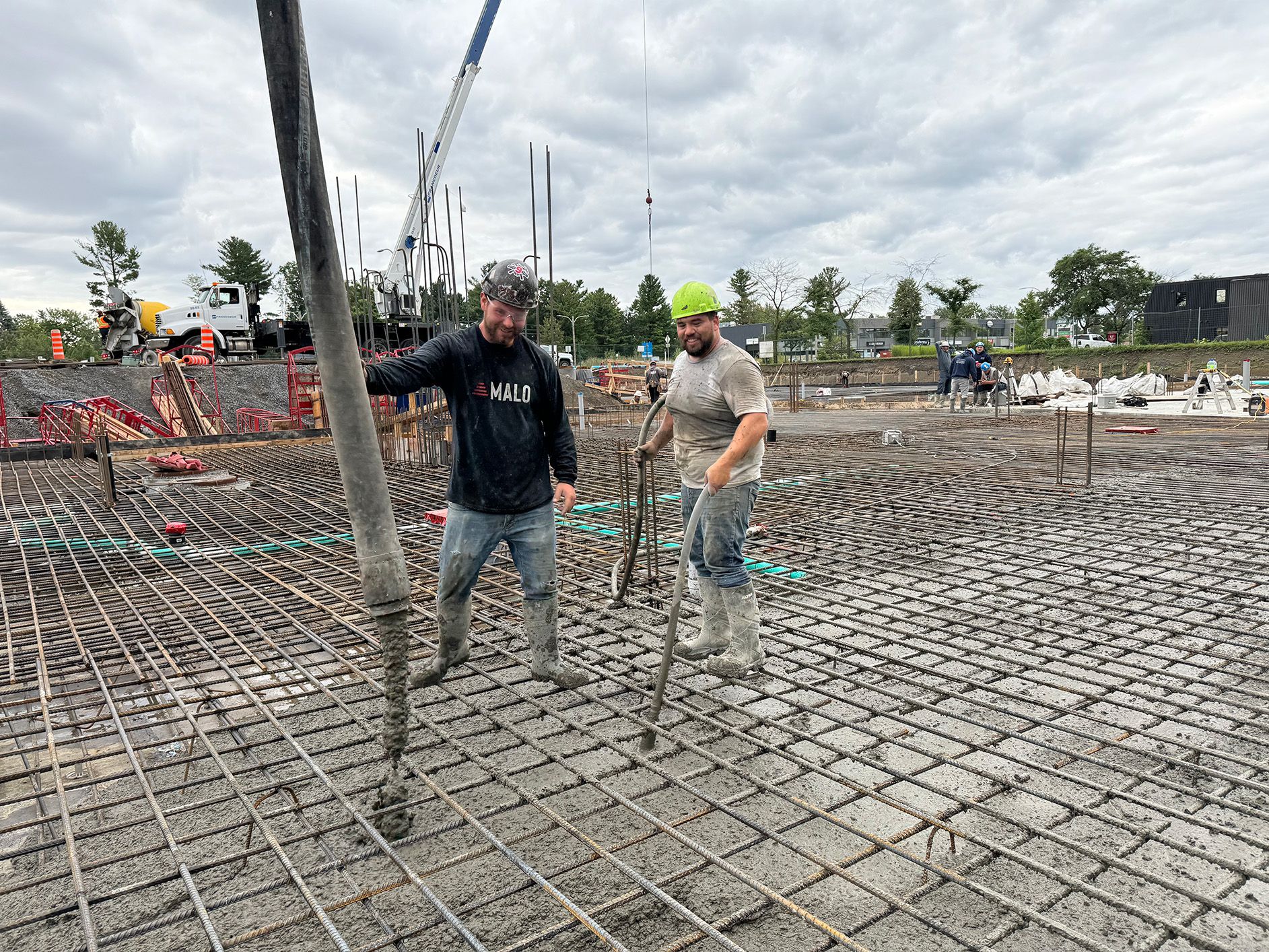 Deux ouvriers du bâtiment coulent du béton sur une armature en fer. Journée nuageuse sur un chantier.