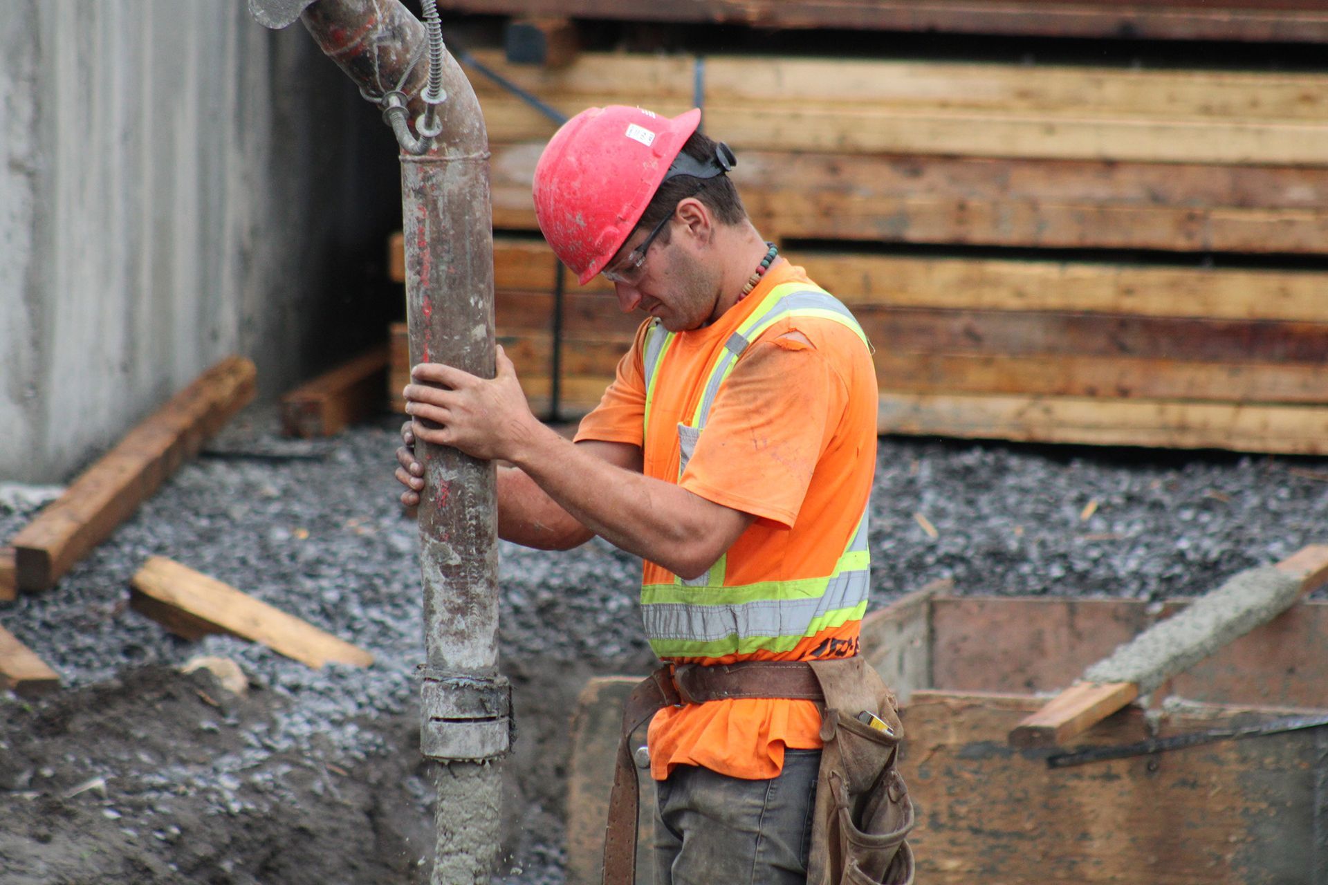 Ouvrier du bâtiment en gilet de sécurité orange et casque rouge, guidant le flux de béton.