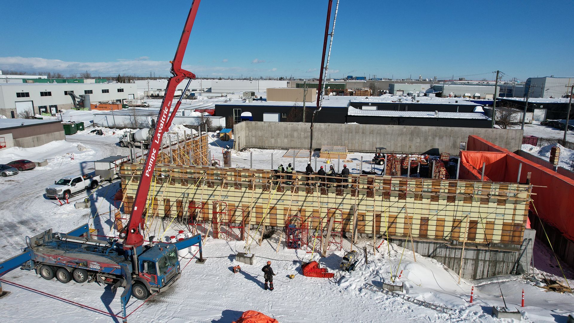 Chantier de construction avec camion-pompe à béton et coffrages en bois, dans un décor enneigé.