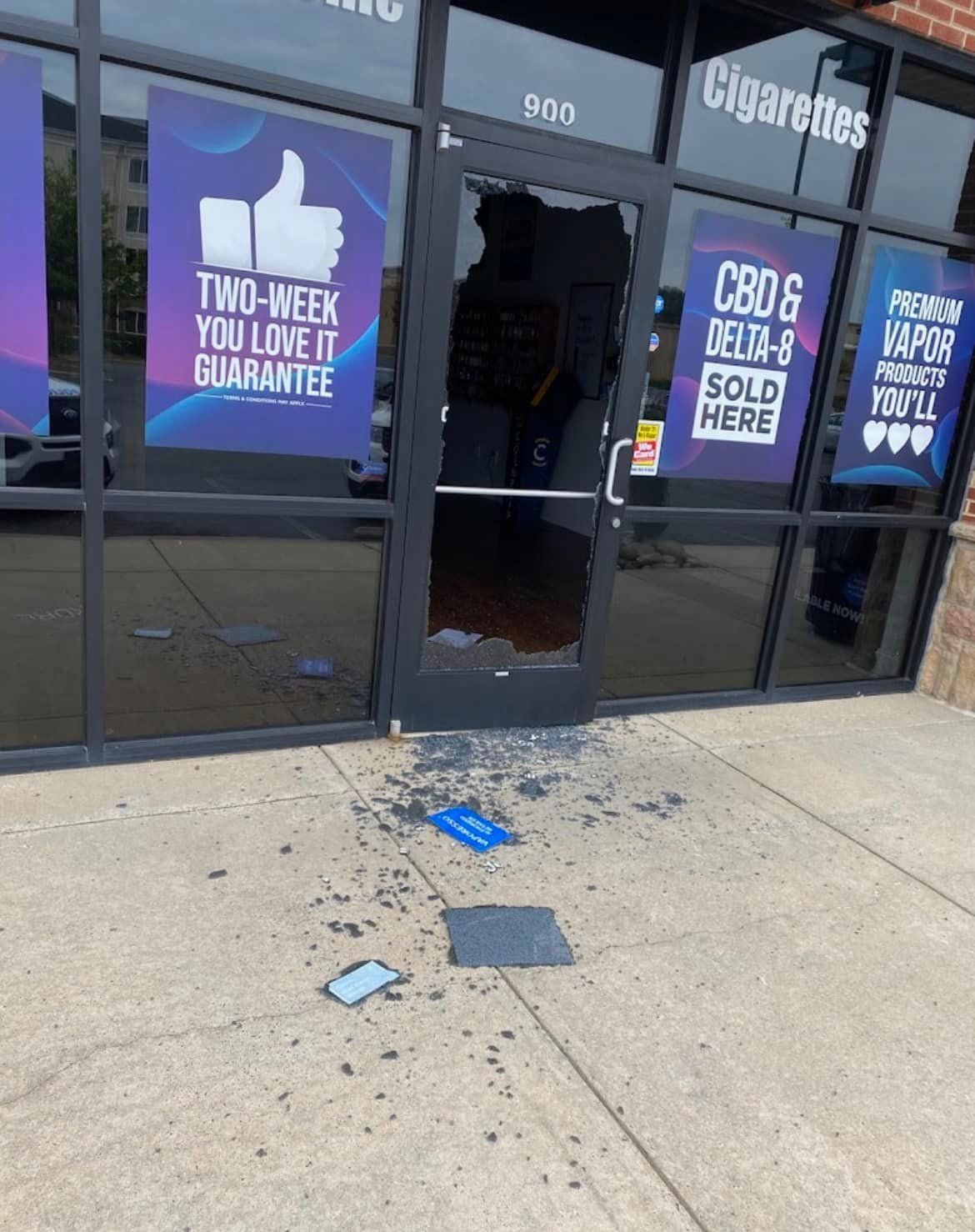 Broken glass door of a vape shop; debris on the sidewalk. 