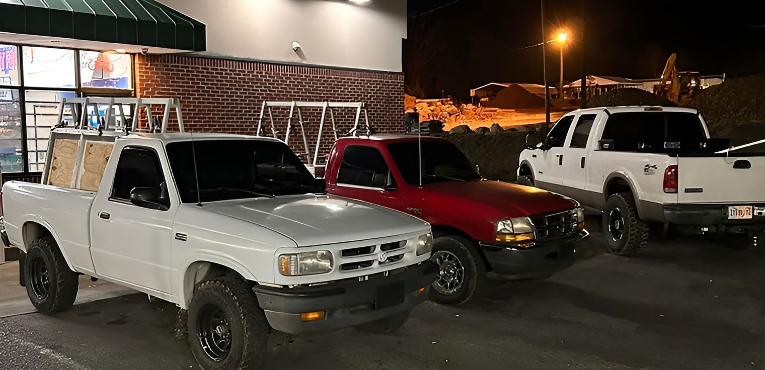 Three pickup trucks parked at night. White, red, and a larger white truck. Building in background.