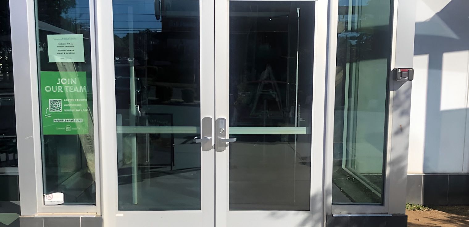 Glass doors with signs, handles, and a white frame, likely for a store entrance.