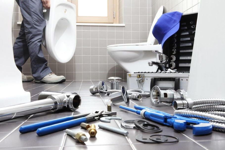 Tools and plumbing parts scattered in a bathroom while a worker repairs a toilet