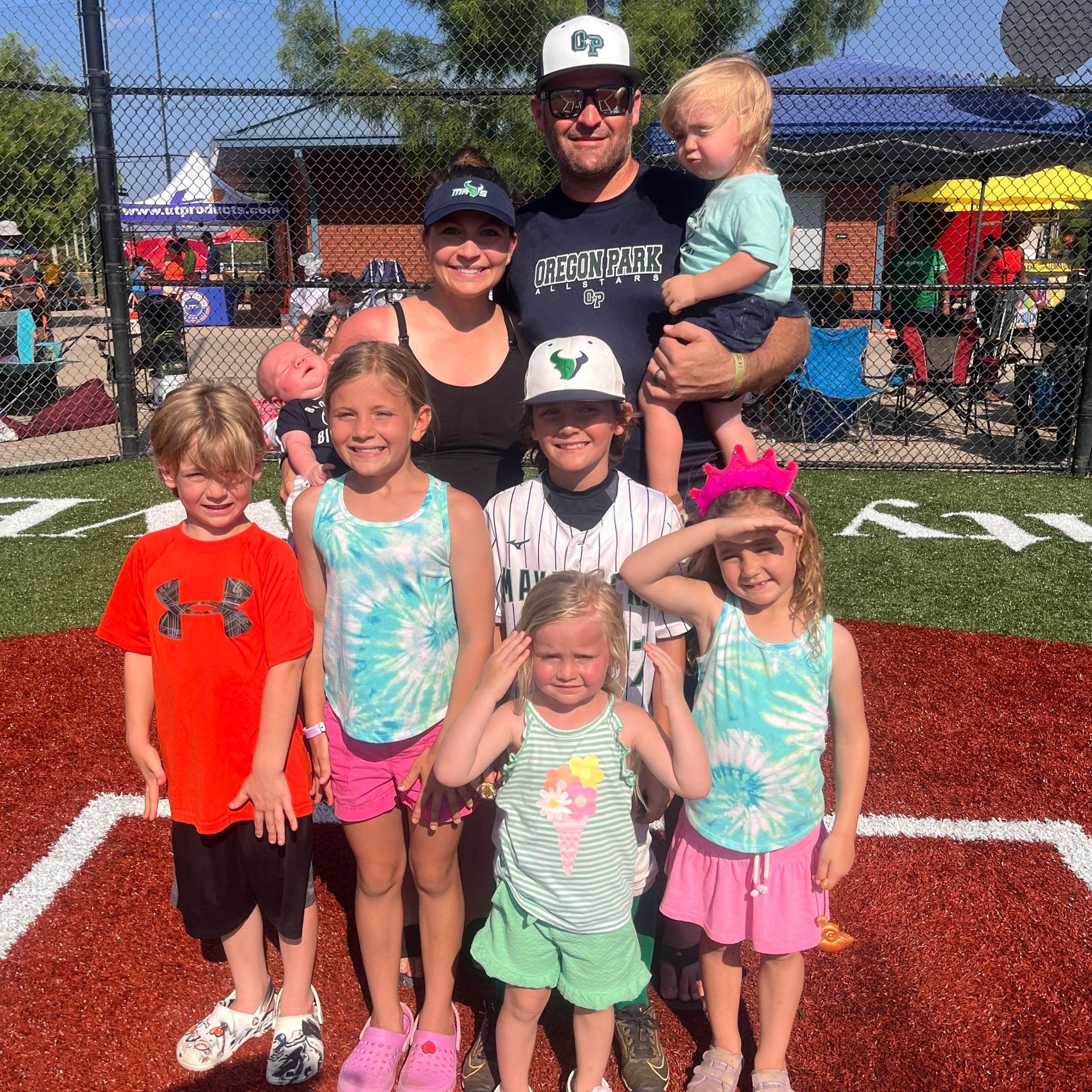 Football coach with arms crossed, standing on a football field. He wears a navy polo shirt and gray pants.