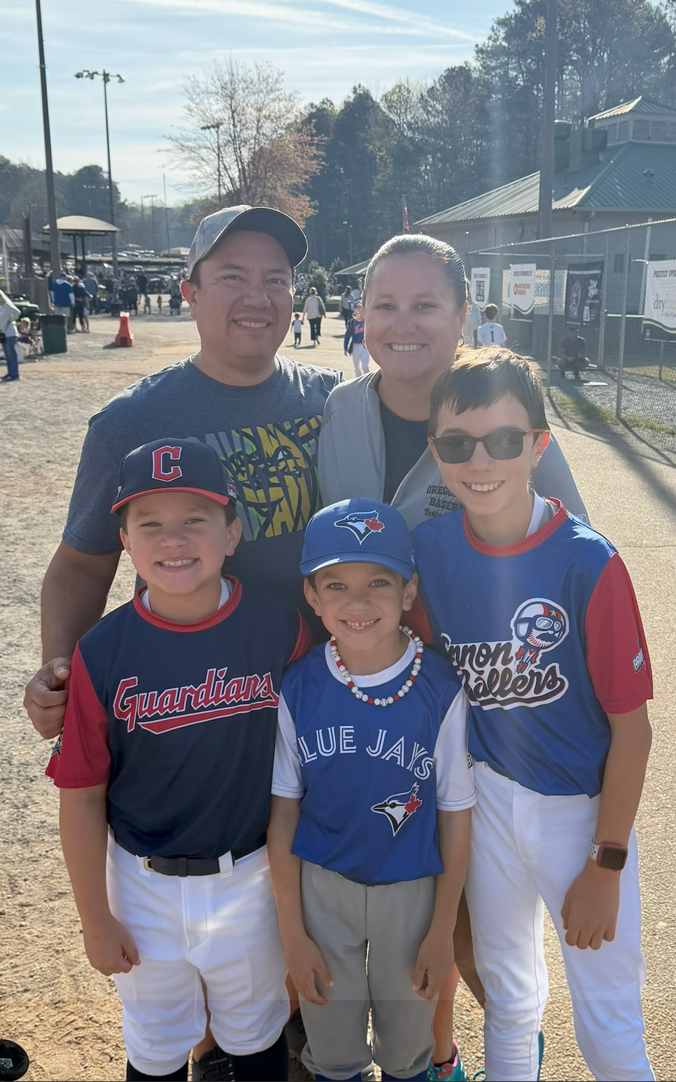 Football coach with arms crossed, standing on a football field. He wears a navy polo shirt and gray pants.