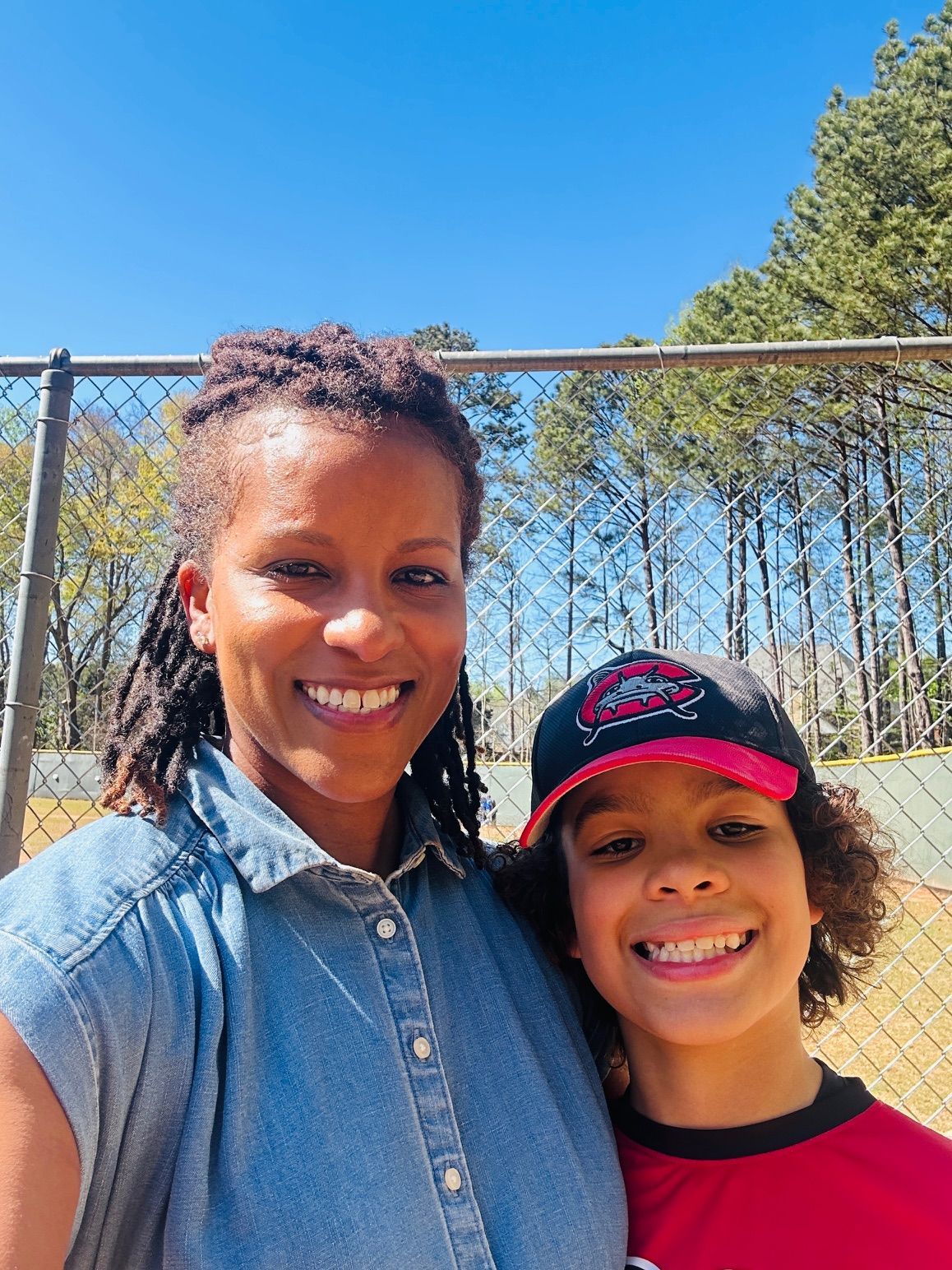Football coach with arms crossed, looking stern on a sunny field, players in the background.