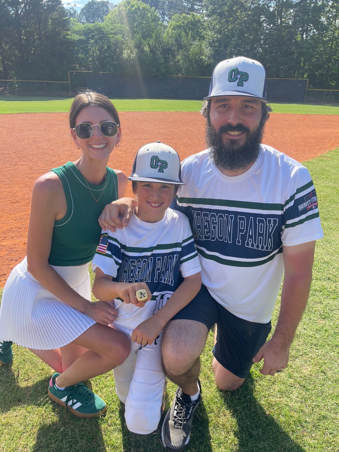 Man in green polo stands on a football field, arms crossed, stadium in background.