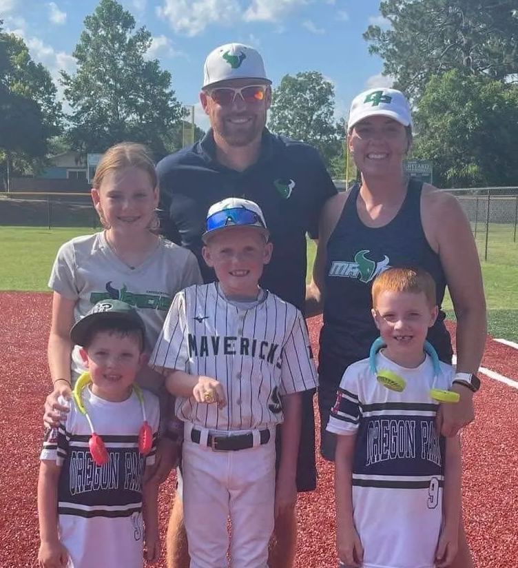 Man in green polo stands on a football field, arms crossed, stadium in background.
