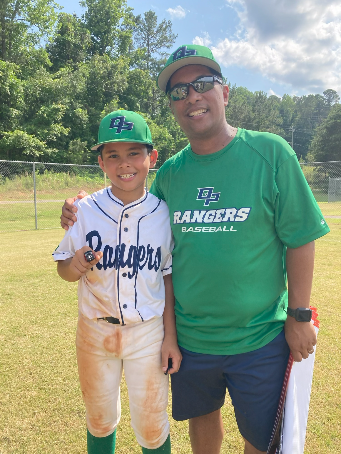 Football coach with arms crossed, standing on a football field. He wears a navy polo shirt and gray pants.