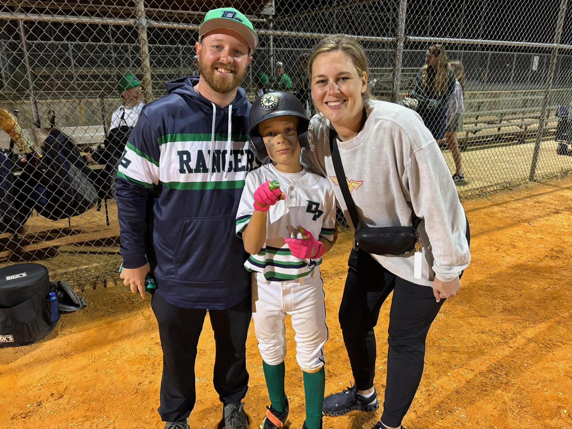 Football coach with arms crossed, looking stern on a sunny field, players in the background.