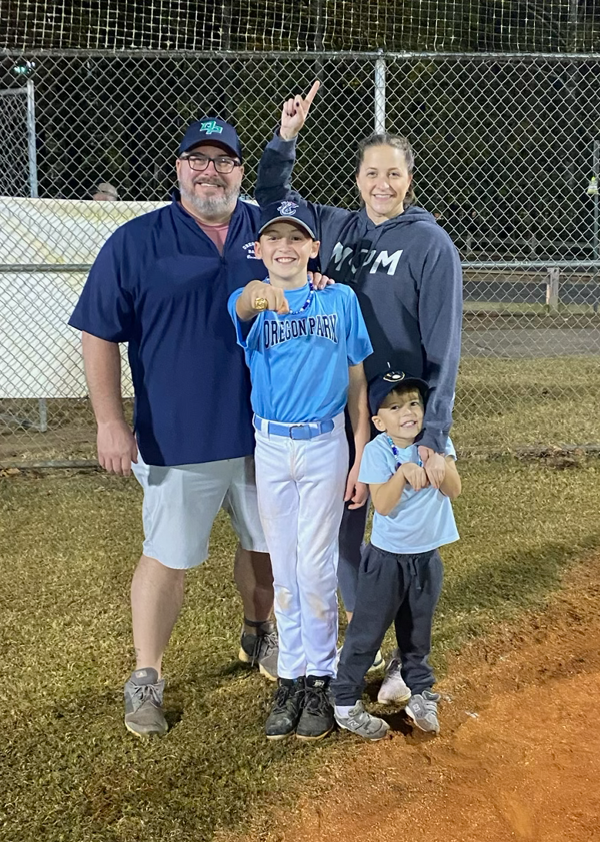 Football coach with arms crossed, standing on a football field. He wears a navy polo shirt and gray pants.