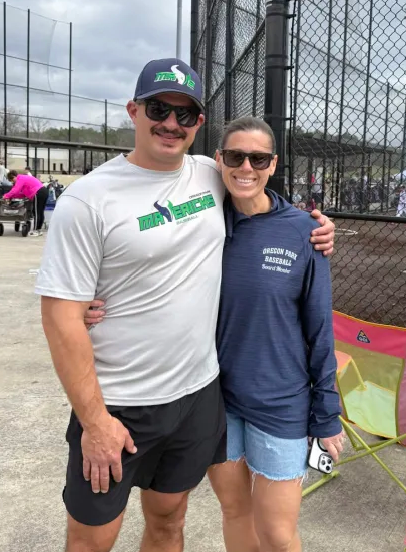Man in green polo stands on a football field, arms crossed, stadium in background.