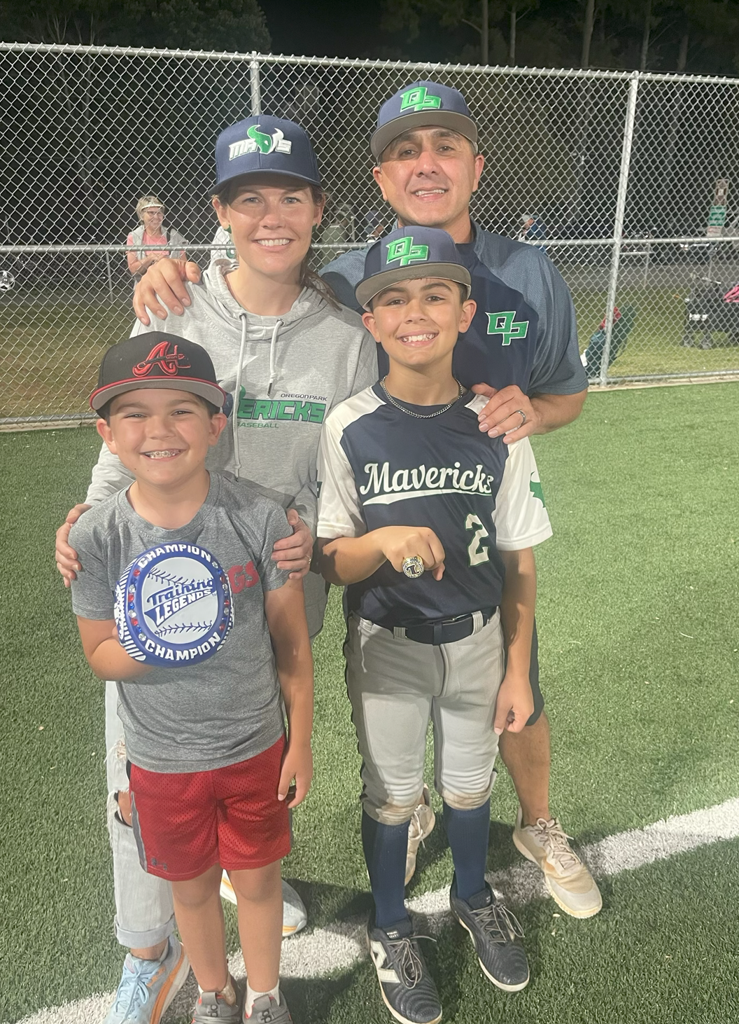 Man in green polo stands on a football field, arms crossed, stadium in background.