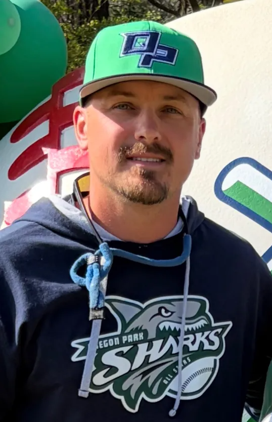 Man in green polo stands on a football field, arms crossed, stadium in background.