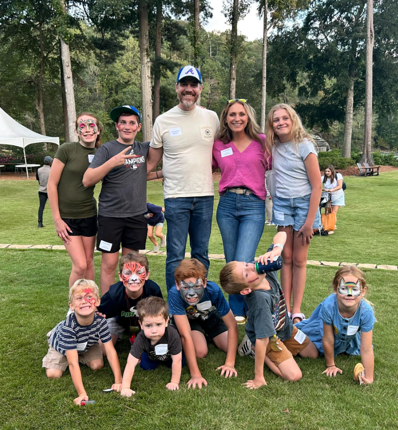 Man in green polo stands on a football field, arms crossed, stadium in background.