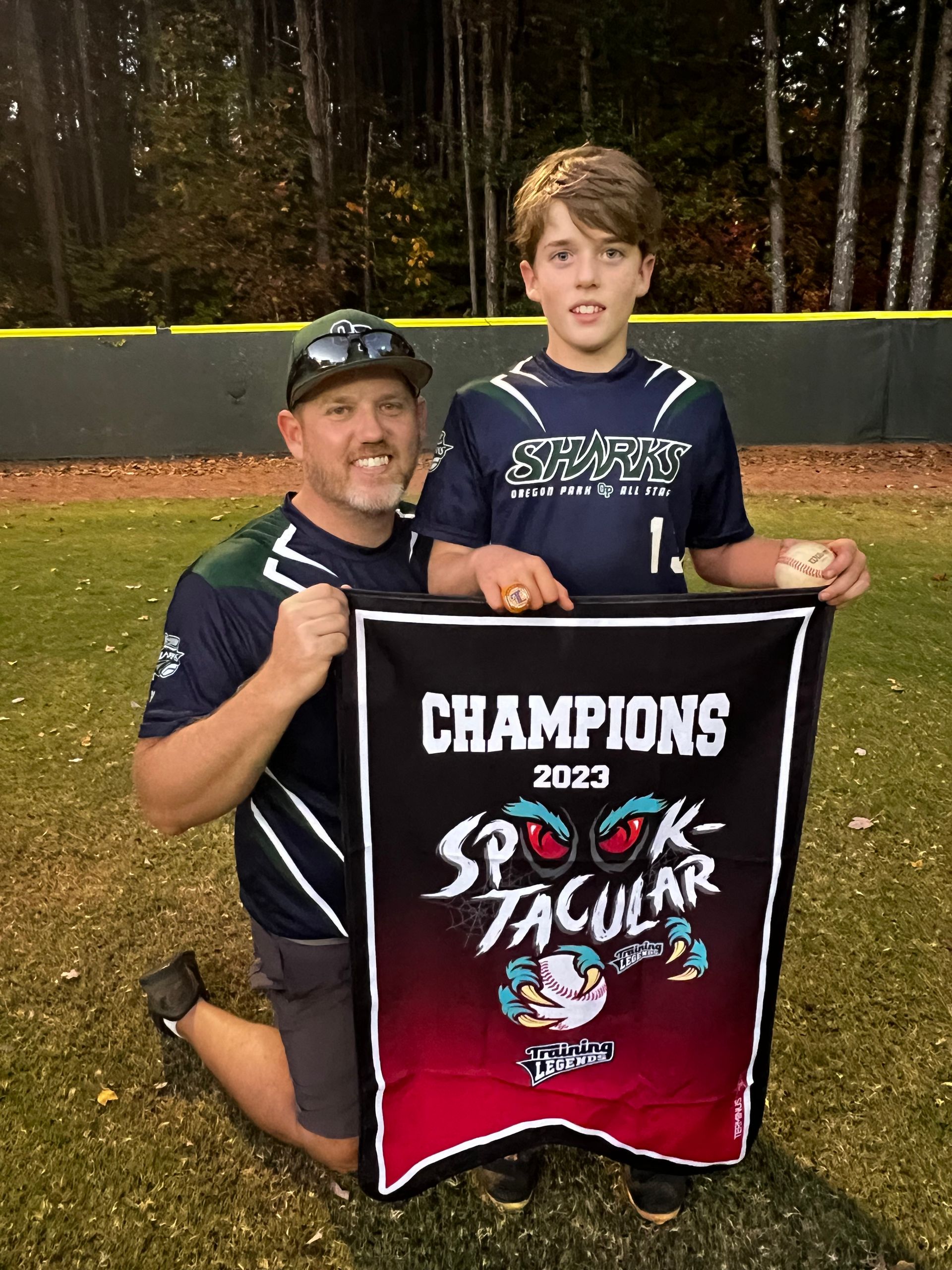 Football coach with arms crossed, looking stern on a sunny field, players in the background.
