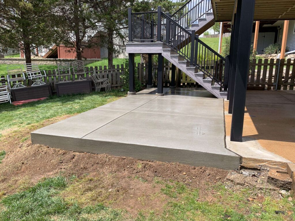 A concrete patio with stairs leading up to a deck in a backyard.