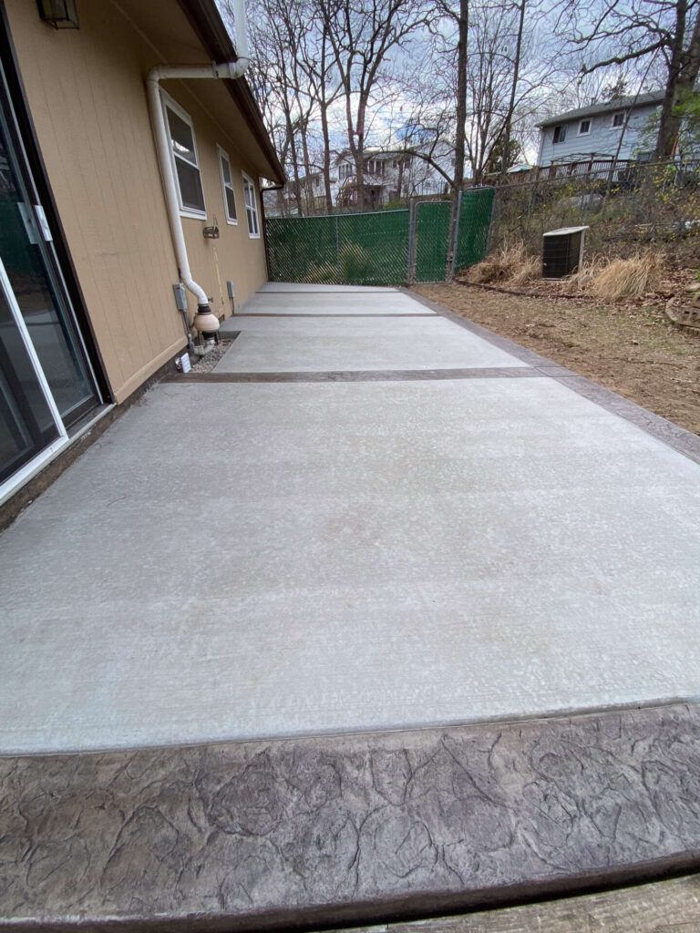 A concrete patio in front of a house with trees in the background.