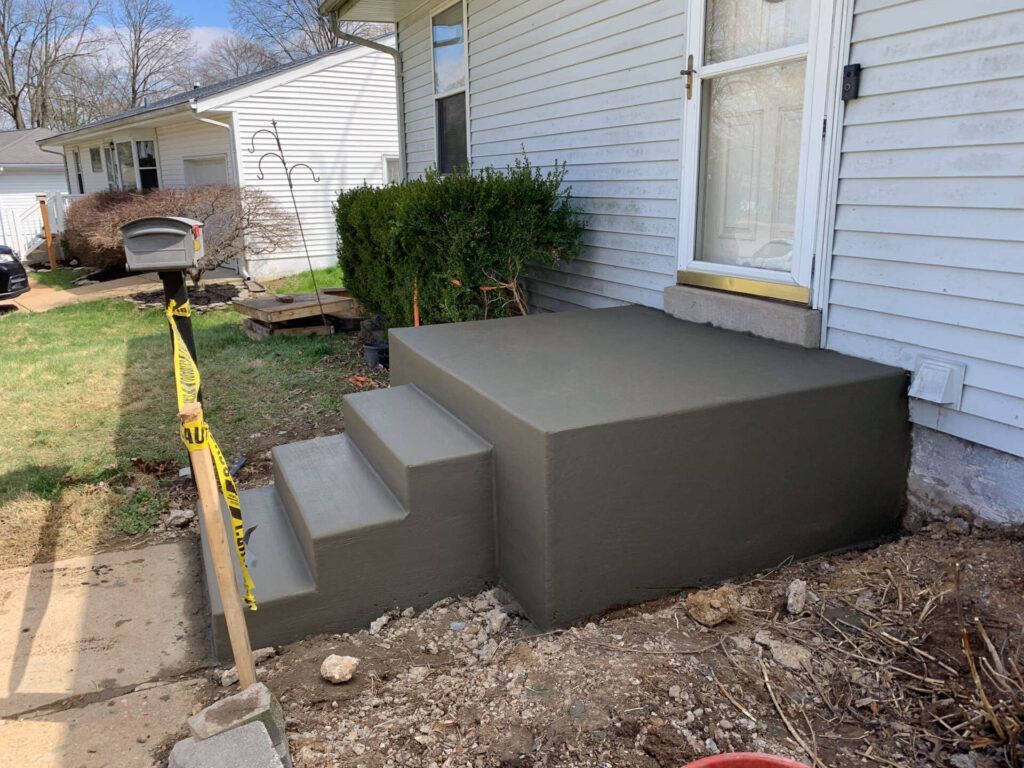 A concrete porch with stairs being built in front of a house.