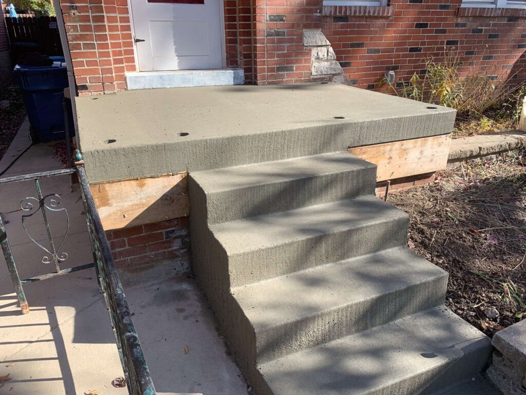 Concrete steps are being built in front of a brick house.