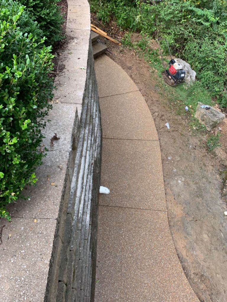 A person is sitting on a rock next to a stone wall on a sidewalk.