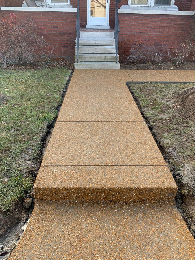 A concrete walkway leading to the front door of a brick house.