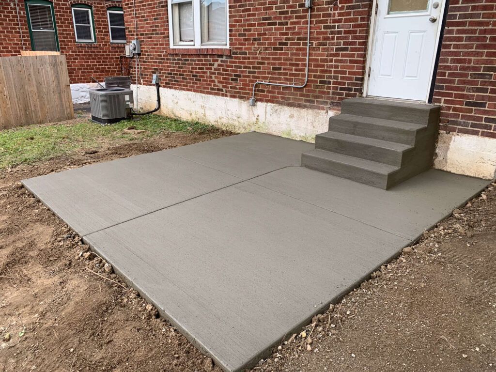 A concrete patio with stairs and a brick building in the background.